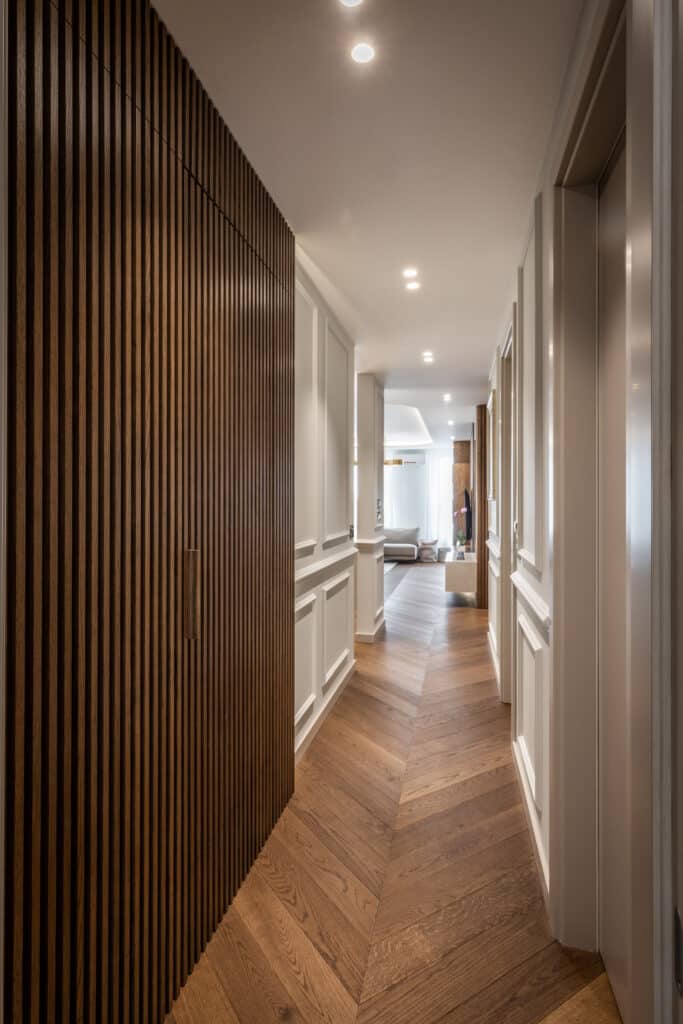 Couloir Moderne : Tasseaux de Bois et Parquet Chevron Couloir moderne avec mur en tasseaux de bois, parquet en chevron et moulures murales blanches élégantes.