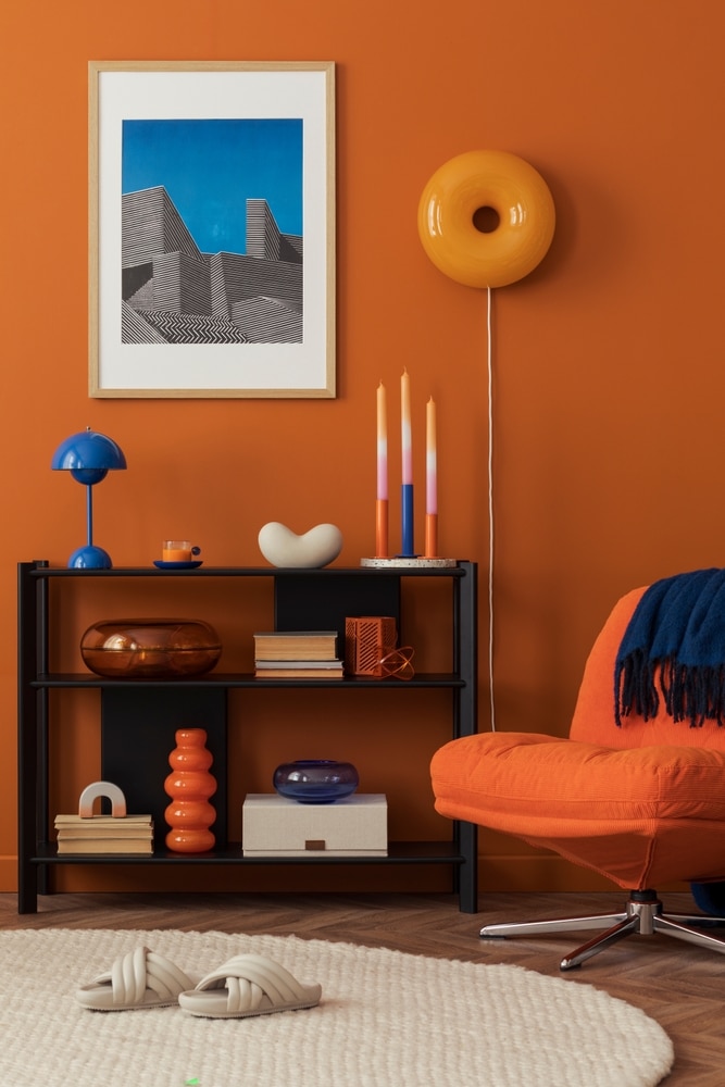Déco Salon Orange et Bleu : Style Moderne et Audacieux Salon moderne au mur orange avec étagère noire, déco bleue, fauteuil design et luminaire donut jaune.