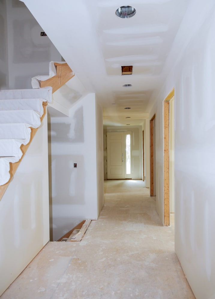 Maison en Construction : Pose de Placo et Finitions Intérieur de maison en travaux : plaques de plâtre jointoyées, escalier protégé et long couloir lumineux.