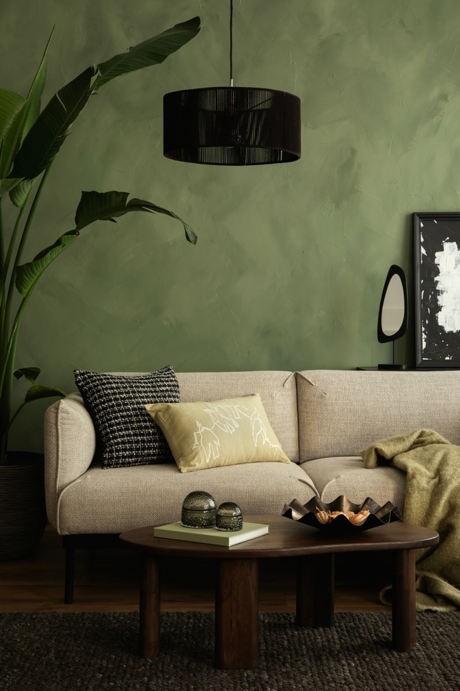 Décoration Salon Moderne : Mur Vert et Canapé Beige Salon moderne avec mur vert texturé, canapé beige, table basse en bois et grande plante verte décorative.